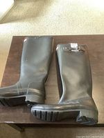 Side view of both black tall rubber boots showing sole tread and adjustable buckle detail.