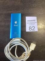 Back view of blue Apple iPod with Apple logo and product info, plus white USB cable coiled next to it