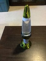 Clear view of the lava lamp with green metallic base and top, showing clear liquid inside and shape of wax.