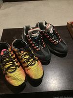 Two pairs of Nike running shoes placed side by side on a dark surface showing the colors and general condition of each pair.