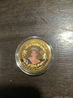 Close-up image of a Princess Diana proof coin with 24K gold plating featuring color portrait and floral designs, set in a clear protective holder.