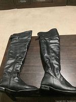 Pair of black thigh high boots laid on a table, showing full side profile of both boots.