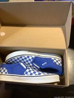 Pair of Vans women's slip-on shoes in blue and white checkerboard pattern inside shoe box.