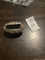 Front angle showing the silver plate body with ornate detailing, lighter top exposed on wooden surface.