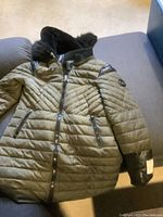 Full view of the olive green woman's winter coat showing front, fur-trimmed hood, and zippered pockets