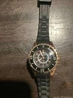 Front view of women's watch showing black dial, gold tone bezel and rubber strap.