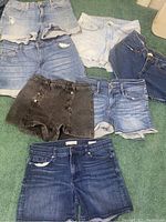 Seven pairs of denim hemmed shorts laid out on green carpet, showing various styles and washes.