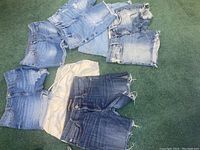 Lot of 7 pairs of cut off denim shorts in various washes and one white pair, all arranged on carpet floor