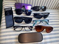 Six pairs of glasses arranged on a fabric surface with two cases, showing the variety of frames and lens types.
