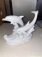 Front angle view of white ceramic dolphin figurine depicting two dolphins leaping out of waves.