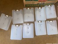 Top view of 9 new plastic ice packs arranged flat in a styrofoam container showing the front face with multiple round bumps and white caps.