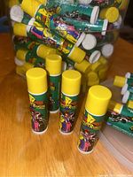 Close up of multiple Power Rangers themed lip gloss tubes with yellow caps and green labels inside a clear plastic tub.