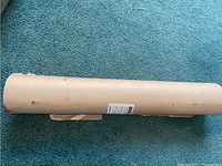 Photo of the new sealed roll of masking paper lying horizontally on a blue carpet showing the full length and cylindrical form