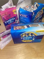 Boxes of Tampax tampons including Radiant and Pocket Pearl displayed with damaged boxes but sealed products inside.