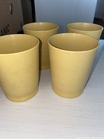 Four yellow cylindrical tumblers standing on a flat surface, showing their smooth outer surfaces.
