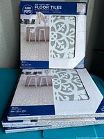 Four boxes of Floor Pops peel and stick floor tiles stacked, packaging shows the tile pattern and quantity (10 tiles per box, 12x12 inch size).