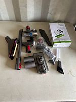 Photo showing Dyson vacuum cleaner accessories including various nozzles, extension wands, brushes, and two boxed Robot Rambo vacuum filters.