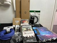 Photo shows two Dell keyboards in boxes, blue and black cables, headphones, DVDs, and a packaged galaxy-themed laptop sleeve.
