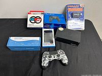 All items displayed on black surface including Nintendo Switch handle steering wheel box, blue wired controller, camouflage wireless controller, Magic Jack Plus device and box, Nintendo Switch dock, game card case, and power supply box.