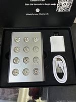 Opened box showing Kala Mini red light therapy device with 12 nodes and included charging accessories in cutout foam packaging.