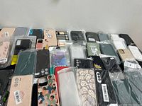Overview image showing a large assortment of new phone cases in various colors and designs, all individually packaged in plastic pouches, arranged on a table.