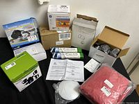 Various lighting and accessory items arranged on a flat surface showing boxed halogen bulb, heated fan ventilator, sensor LED lights in green packaging, and other boxed electrical components.