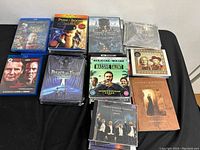 Photo showing Blu-rays, DVDs, and CDs arranged on a black surface with visible titles including Puss in Boots, Magic Mike double feature, and Massive Talent