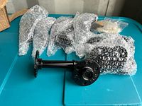 Set of six black metal shelving pipes, some pieces wrapped in bubble wrap, laid out on blue surface with mounting hardware in plastic bag.