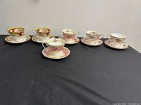 Full display of six Royal Albert bone china tea cups and saucers in three different patterns arranged on black fabric.