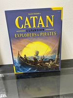 Front of the boxed Settlers of Catan Explorers & Pirates Expansion board game showing title and artwork.