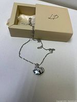 Sterling silver heart necklace with blue gemstone pendant laid next to a cream-colored box with 'LP' written on the lid.
