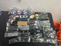 Overall view of multiple sunglasses individually wrapped in plastic with several black cases and accessories on a black surface