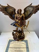 Front and angled view of Adriel bronze sculpture with wings, bow and standing on hand-shaped base, inside protective packaging.