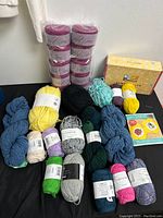 Wide view showing yarn skeins in various colors and sewing kits on black surface.