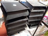 Two stacks of five black wooden display stands each, showing the top felt side with a candle label and the side with a lip edge.