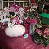 Photo of the lot showing two ceramic vintage floral vases (one cream, one gray) with assorted faux flower stems arranged inside and extra faux palm leaves on side.