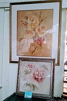 Framed wall art featuring beige-orange roses and the word 'Paix' with a wood-toned frame, and a second framed print of pink flowers in an ornate silver frame
