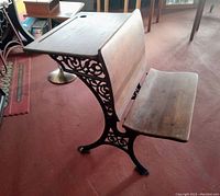 Side angle photo of antique wood student desk with cast iron ornate base and attached bench seat