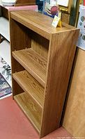 Side angle view of brown wooden 4-shelf bookcase showing wood grain laminate finish and full height.