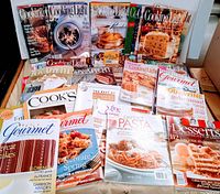 Photo showing the collection of cooking magazines in a box on a table, includes Cooking Light, Bon Appetit, Gourmet, Cook's, and others.
