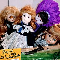 Four vintage porcelain dolls in a box, close-up frontal view showing faces, outfits, and hair styles