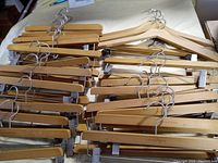 Overview of the full lot showing multiple wooden hangers laid in overlapping stacks on a table, including pant/skirt hangers with clips and contoured top hangers.
