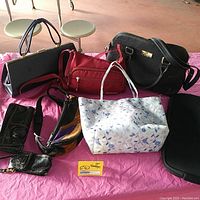 Seven vintage handbags and pouches displayed on pink paper, various colors including black, red, and floral.