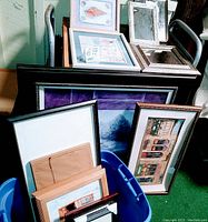 Large and small picture frames grouped inside and next to a blue plastic tub with artworks and backing boards visible, showing frame variety and condition.