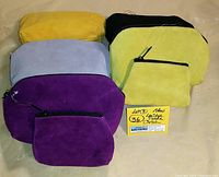 Top-down view of five suede leather clutches in various colors - purple, gray, gold yellow, black, and mustard yellow. Front coin pouches and top zippers visible.