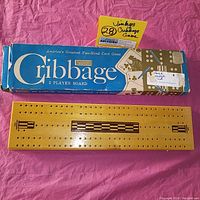 Wooden cribbage board displayed next to original blue box with pegs visible.