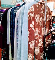 Side view of 9 garments on hangers including rust floral jacket and pastel blue and check patterned garments