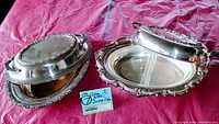 Two vintage silver plate serving dishes with lids, one containing a divided glass bake insert. Ornate handles and edges visible.