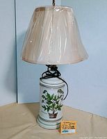 Full view of vintage ceramic table lamp with beige plastic-wrapped shade, showing the entire lamp and electrical cord.
