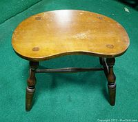 Top view of wooden kidney-shaped seat stool with visible wear and four circular plugs on seat securing it to legs
